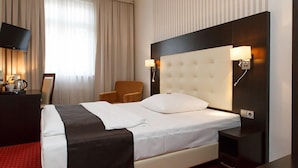 A hotel room with a large bed, a TV, a chair, and a desk with a lamp. - Hotel Herbst Berlin (Berlin)