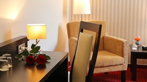 A hotel room with a wooden desk, a lamp, two red roses, a chair, and a striped curtain. - Hotel Herbst Berlin (Berlin)