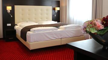 A hotel room with a large bed, two bedside lamps, a red carpet, and a vase with flowers on a table.
