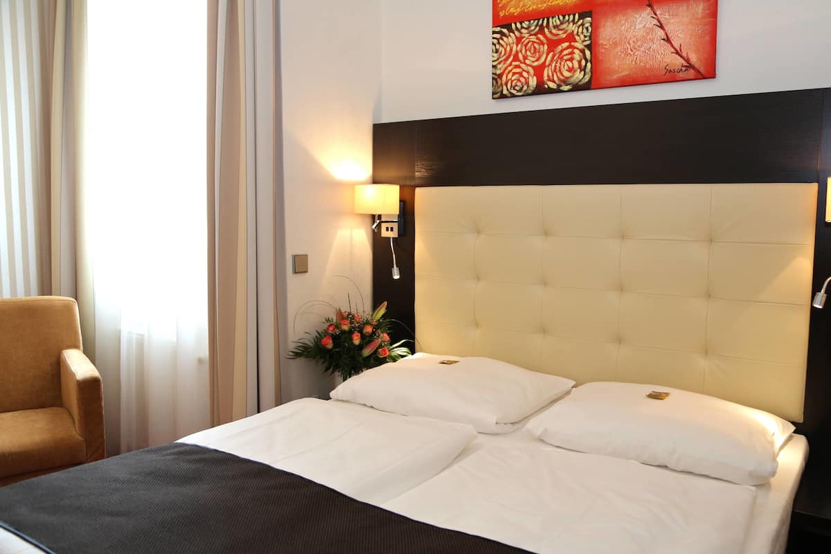 A hotel room with a large bed, a chair, a wall-mounted lamp, and a decorative painting.