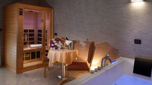 A room with a wooden sauna, a table with flowers, a chair, and a bathtub with a faucet. - Royal Hotel Montevergine (Ospedaletto D'Alpinolo)