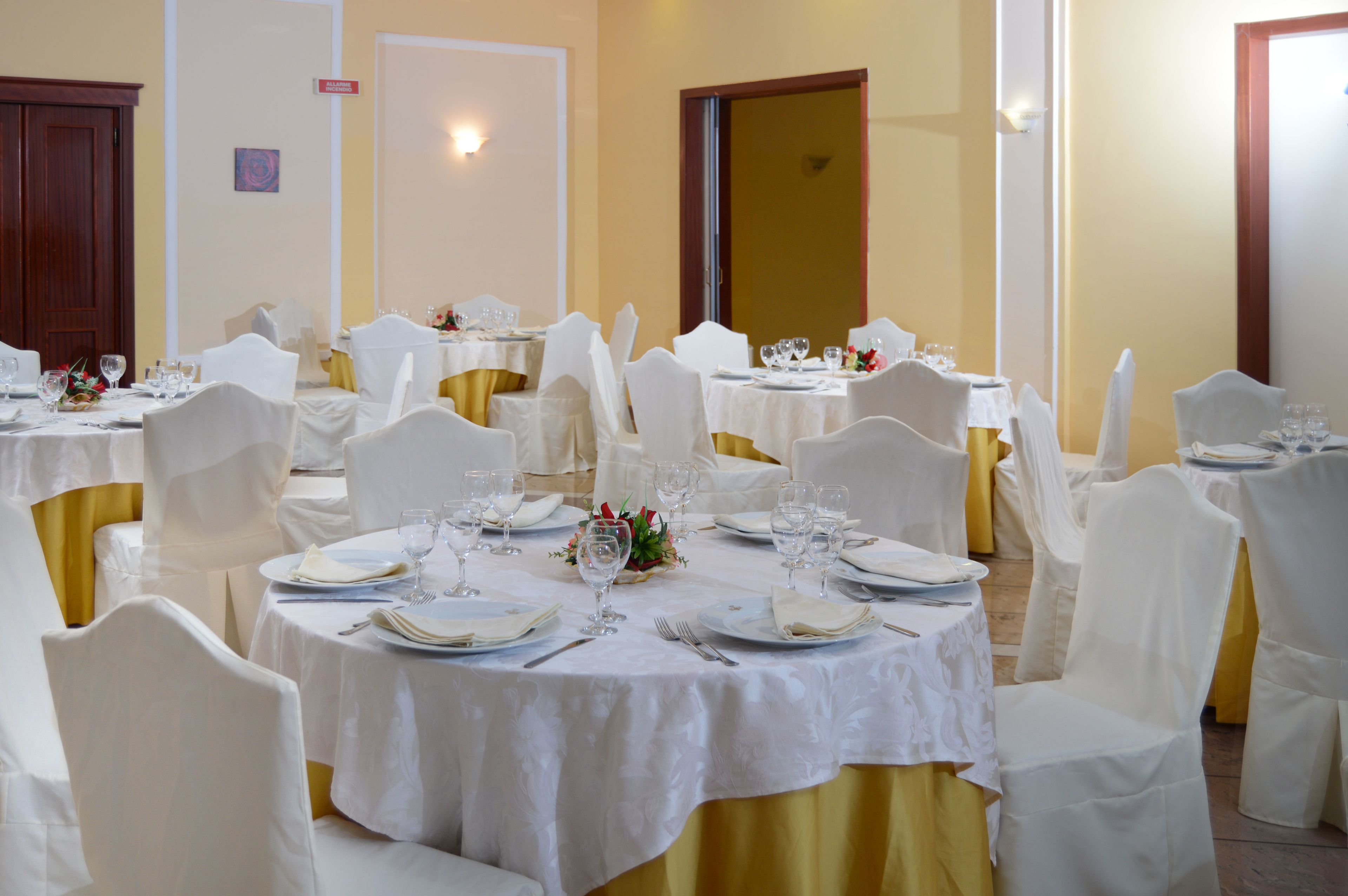 Un salón de banquetes con mesas redondas dispuestas para cenar, sillas blancas y cintas amarillas.