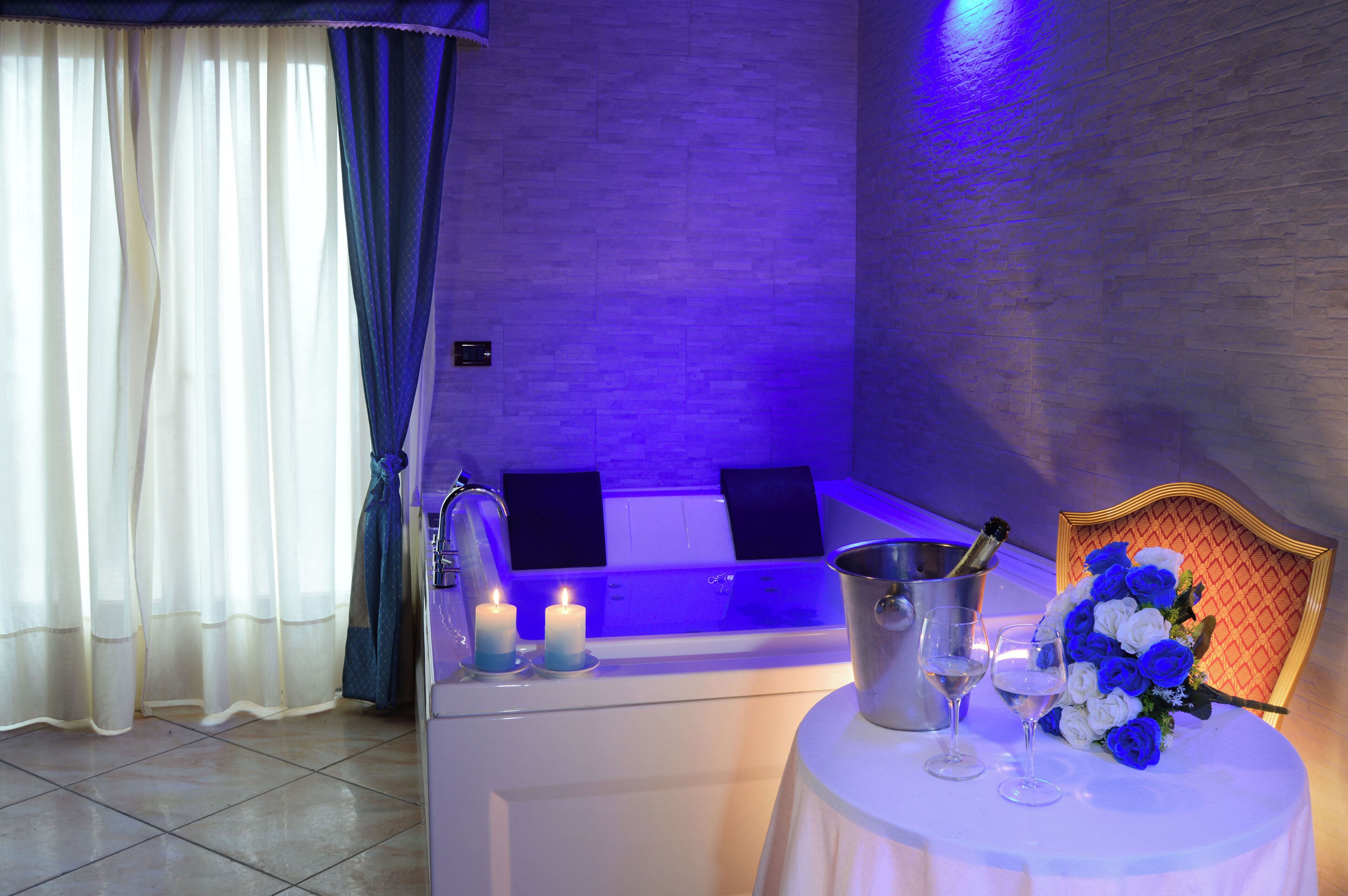 Ett spa-rum med en massagestol, ett bord med en blomsterbukett, ljus och en kylfull flaska champagne.