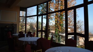 A restaurant with large windows, tables set for dining, and a view of trees and buildings. - Royal Hotel Montevergine (Ospedaletto D'Alpinolo)