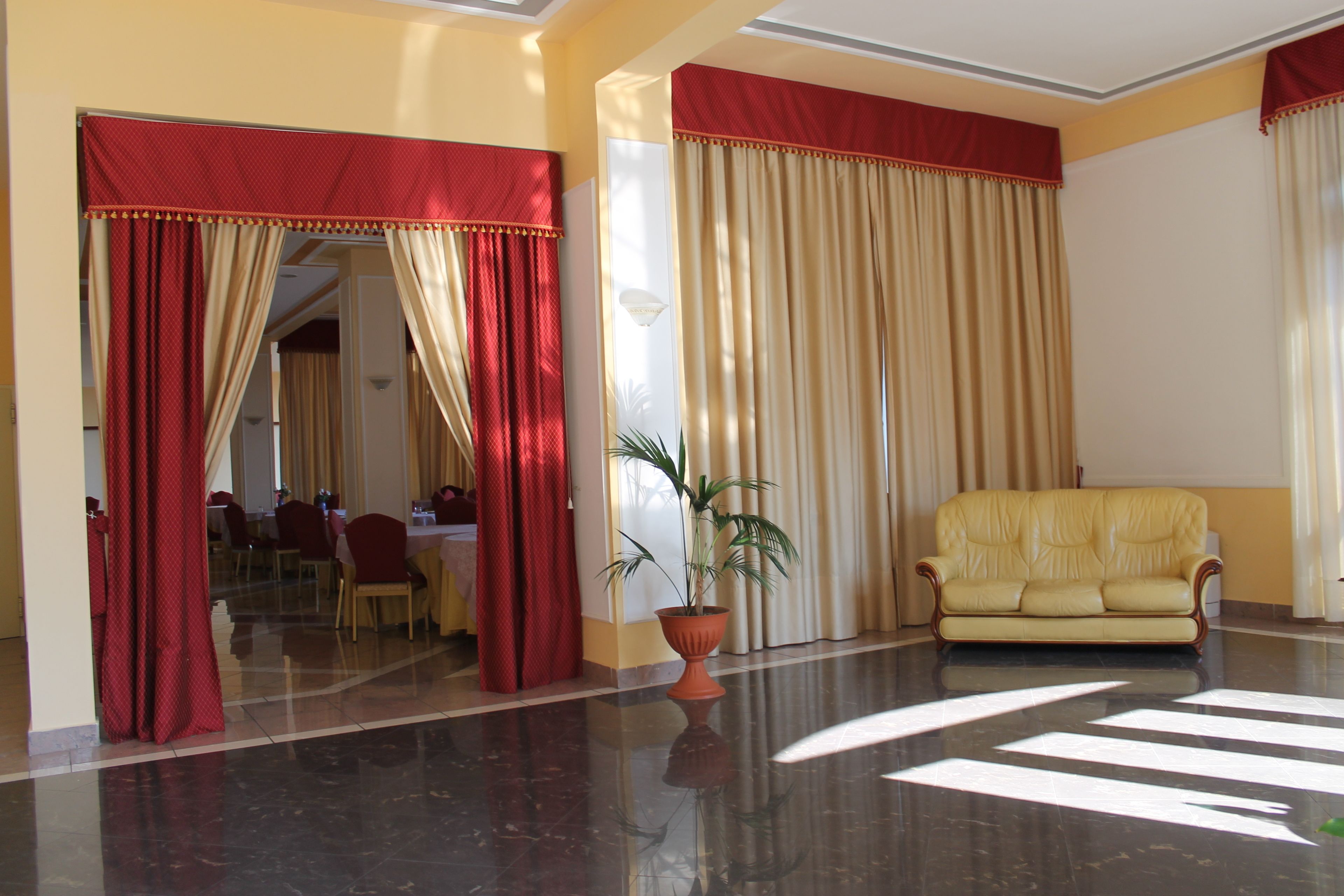 Un vestíbulo con piso reflectante, un sofá amarillo y cortinas rojas y beige.