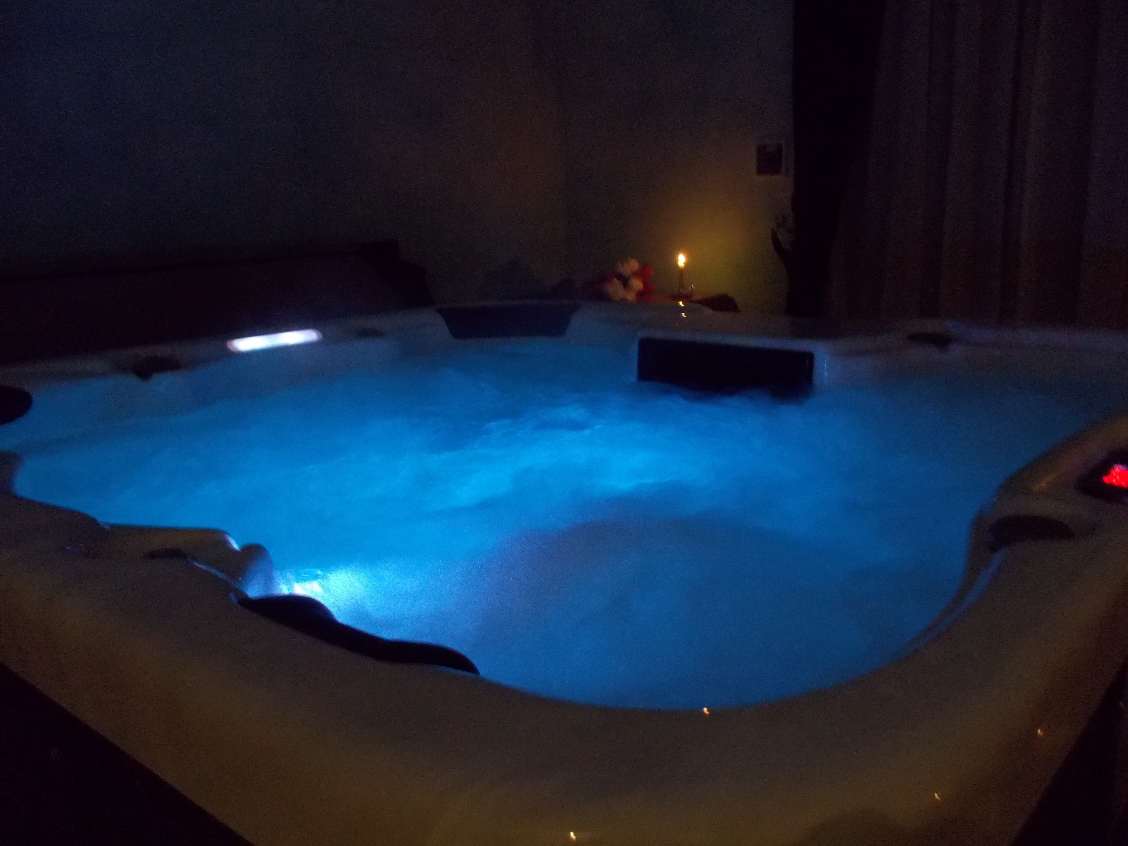 Un bain à remous éclairé d’une lumière bleue, entouré de murs sombres et doté d’un mobilier minimaliste.