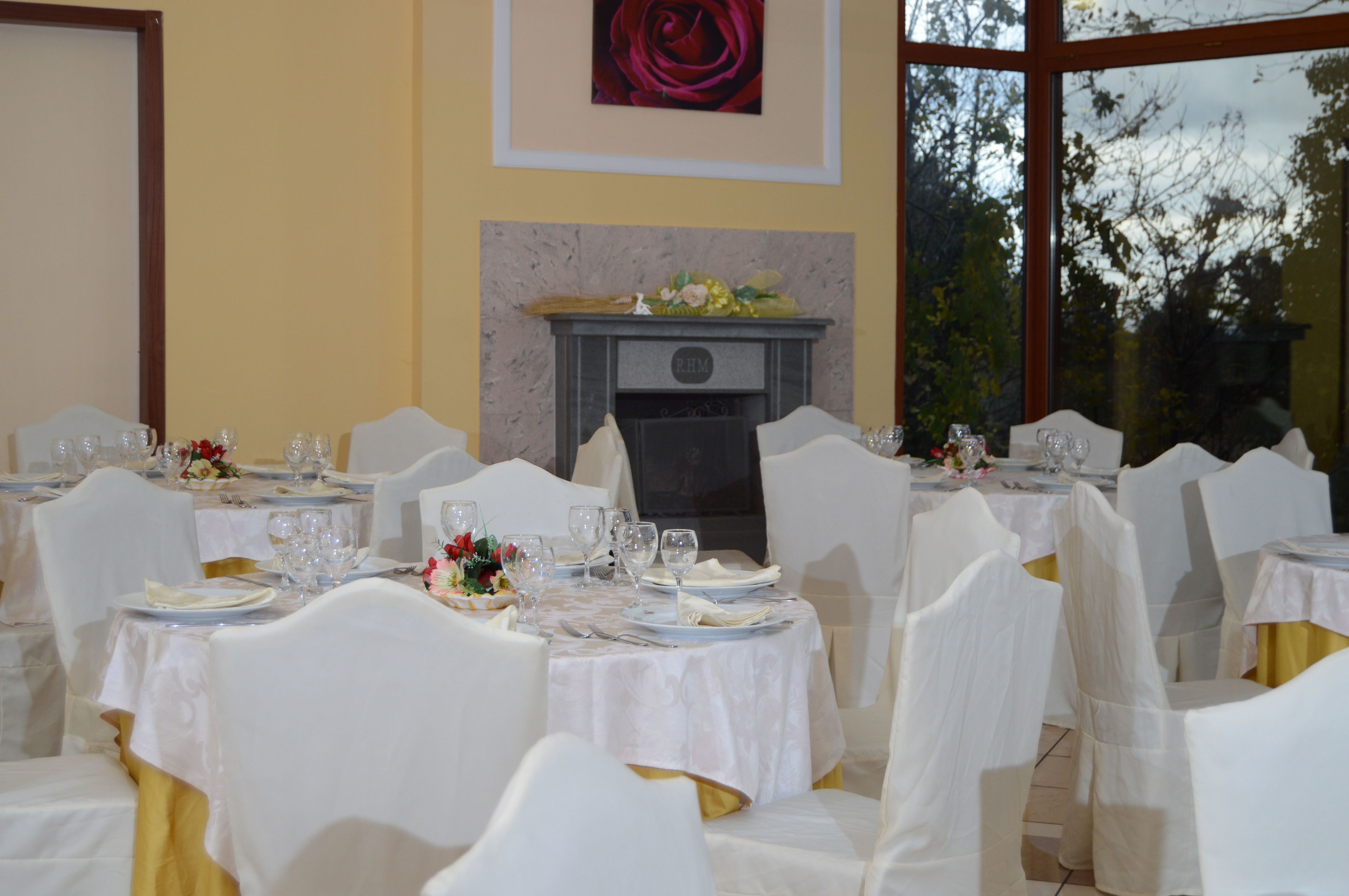 A banquet hall with round tables, white chairs, and a fireplace.