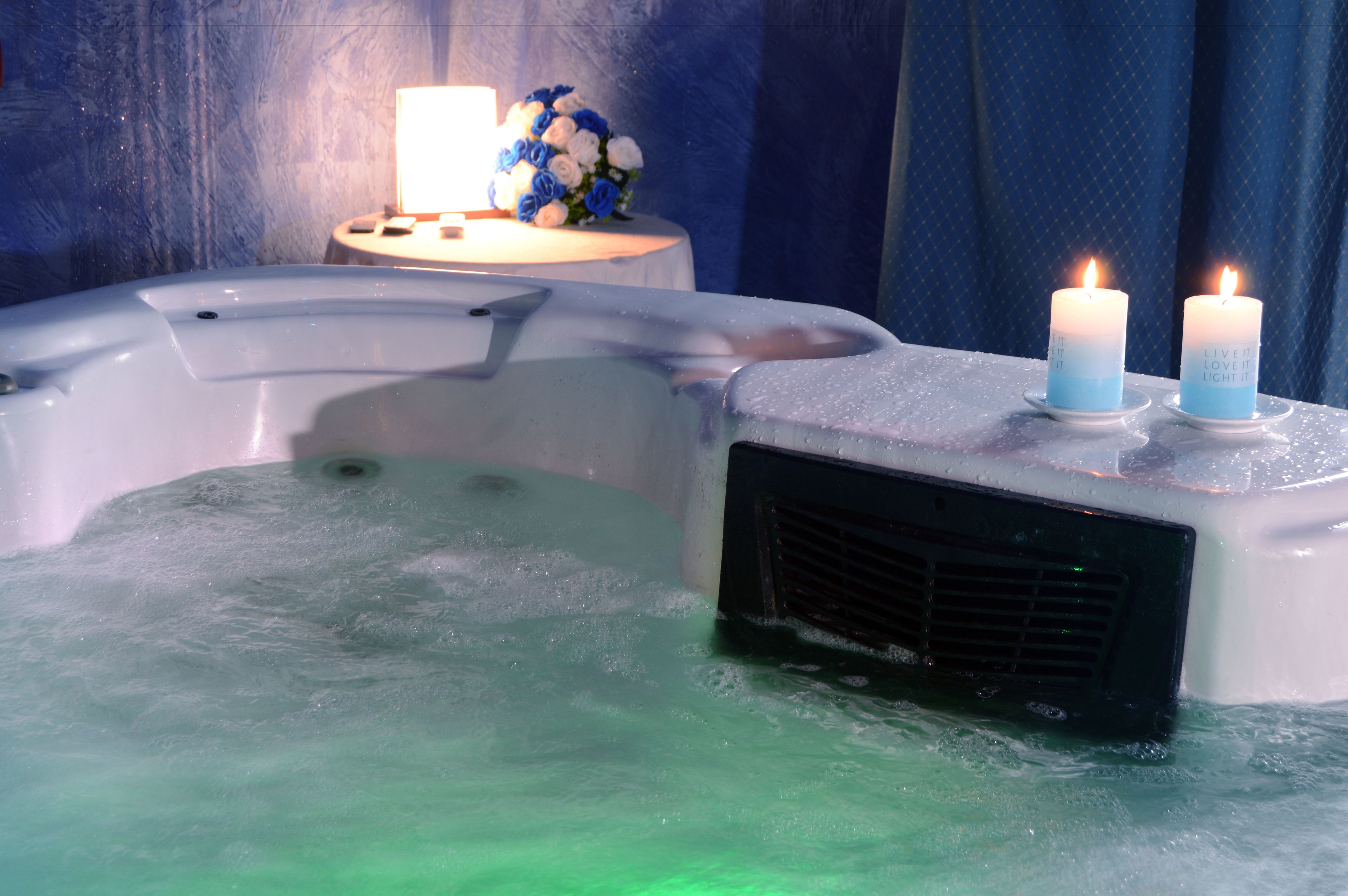 A hot tub with two lit candles and a bouquet of flowers on a side table.