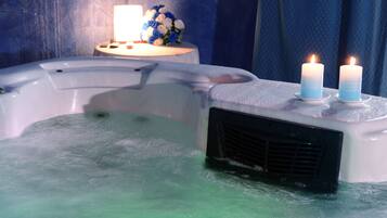 A hot tub with two lit candles and a bouquet of flowers on a side table.
