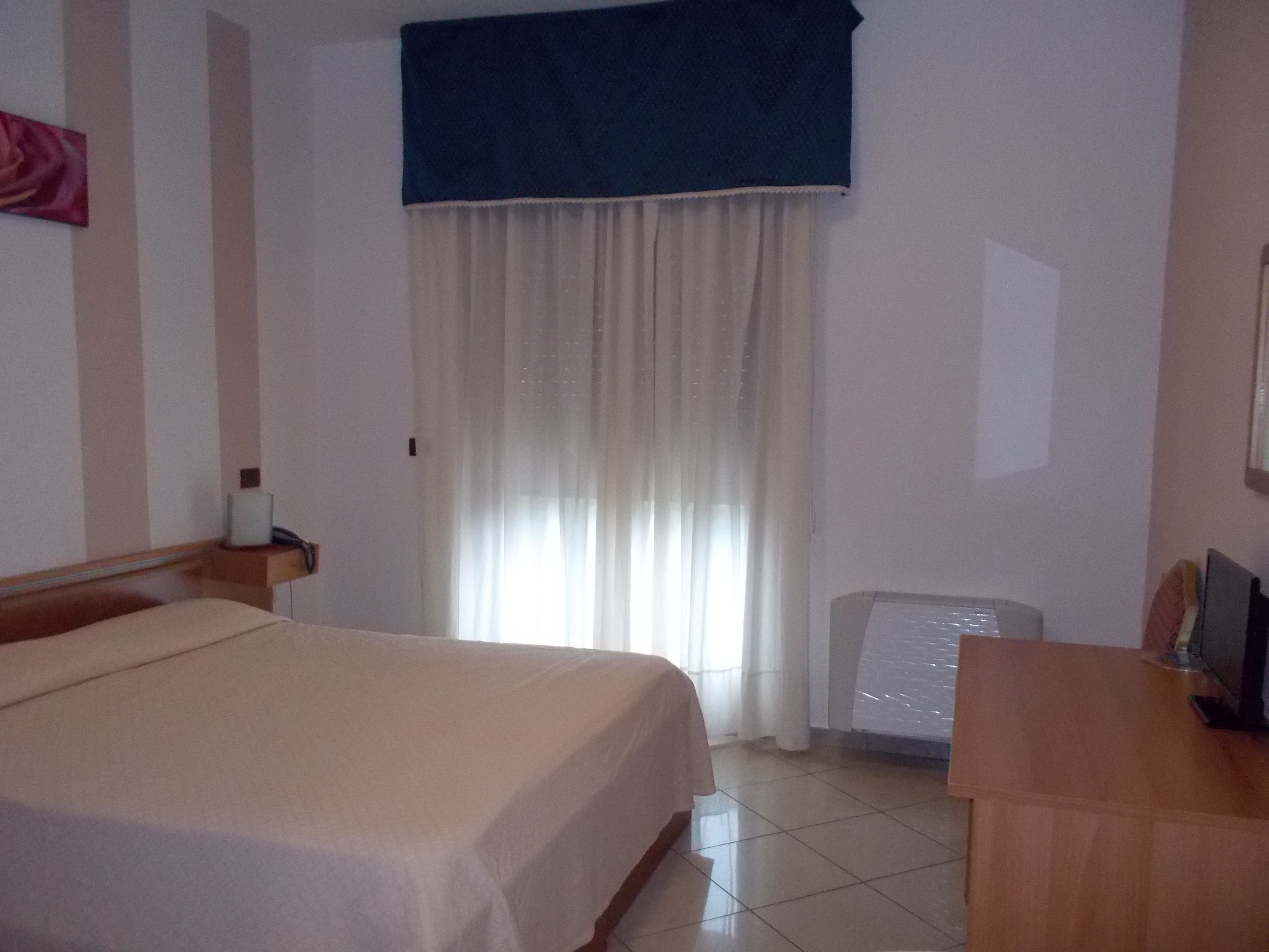 A hotel room with a bed, a desk, a chair, and a window with curtains.