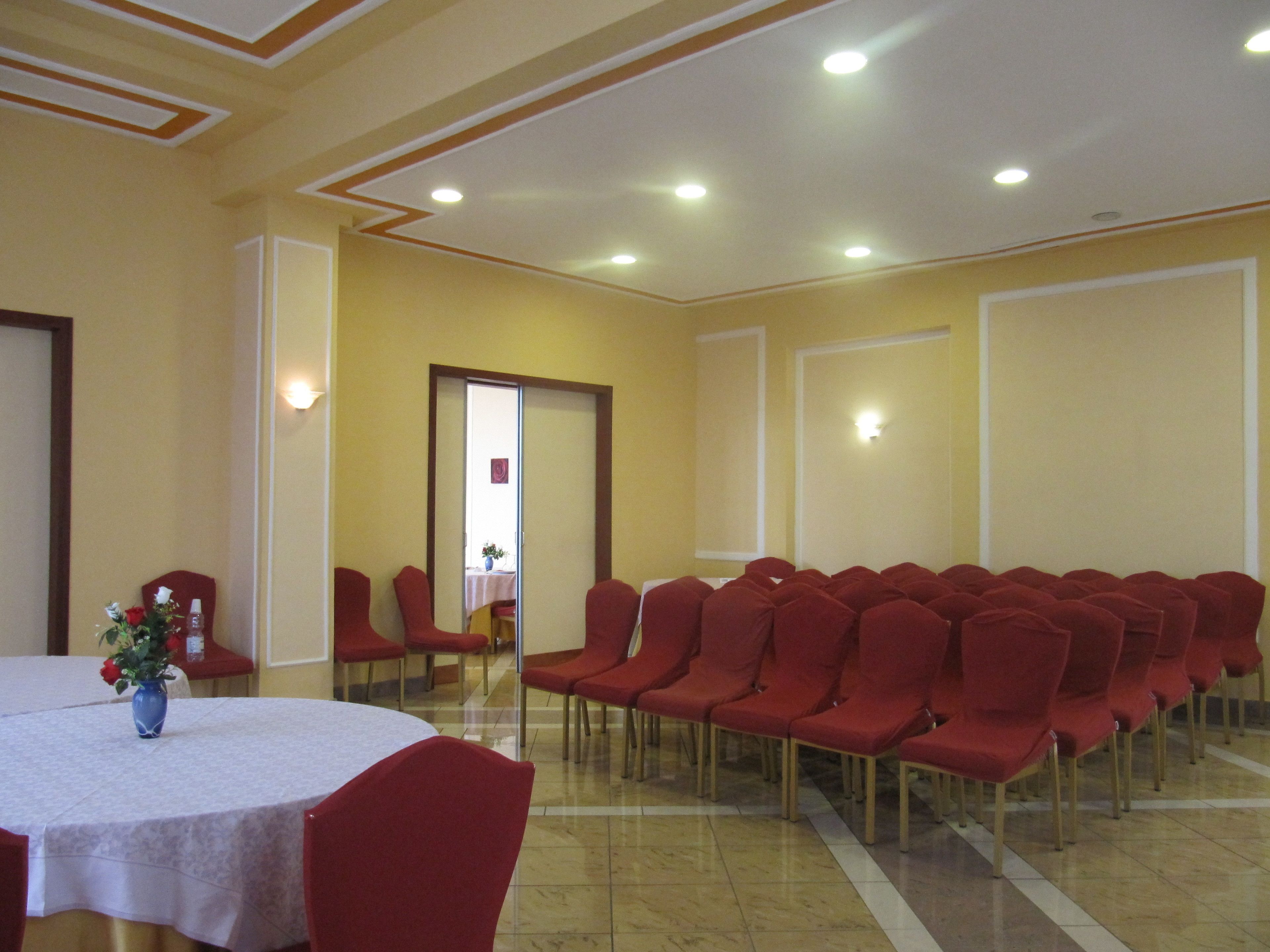 A conference room with rows of red chairs, a round table with a white tablecloth, and a vase of flowers.