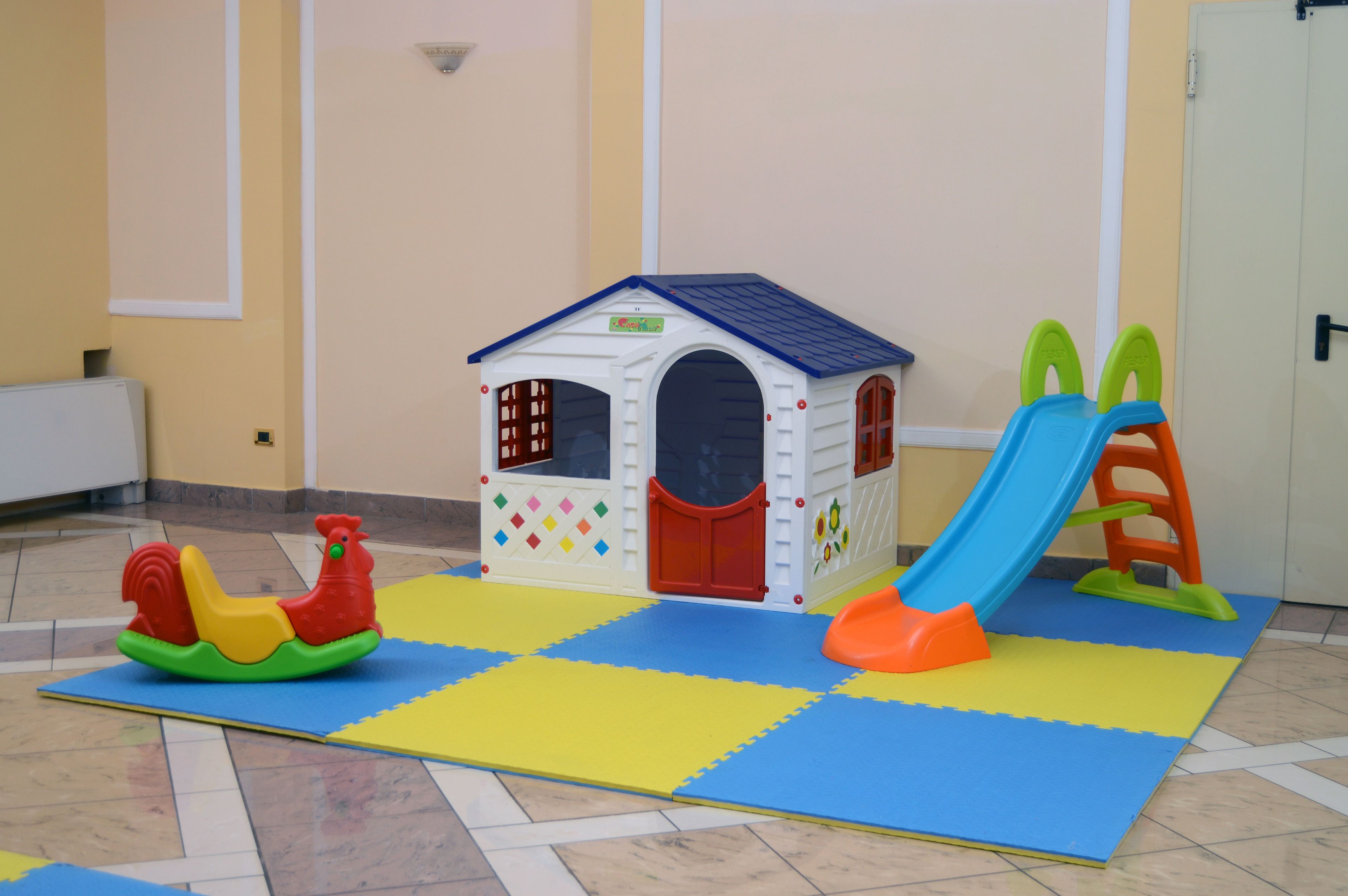 Un área de juegos con una casita, un tobogán y un caballo balancín.