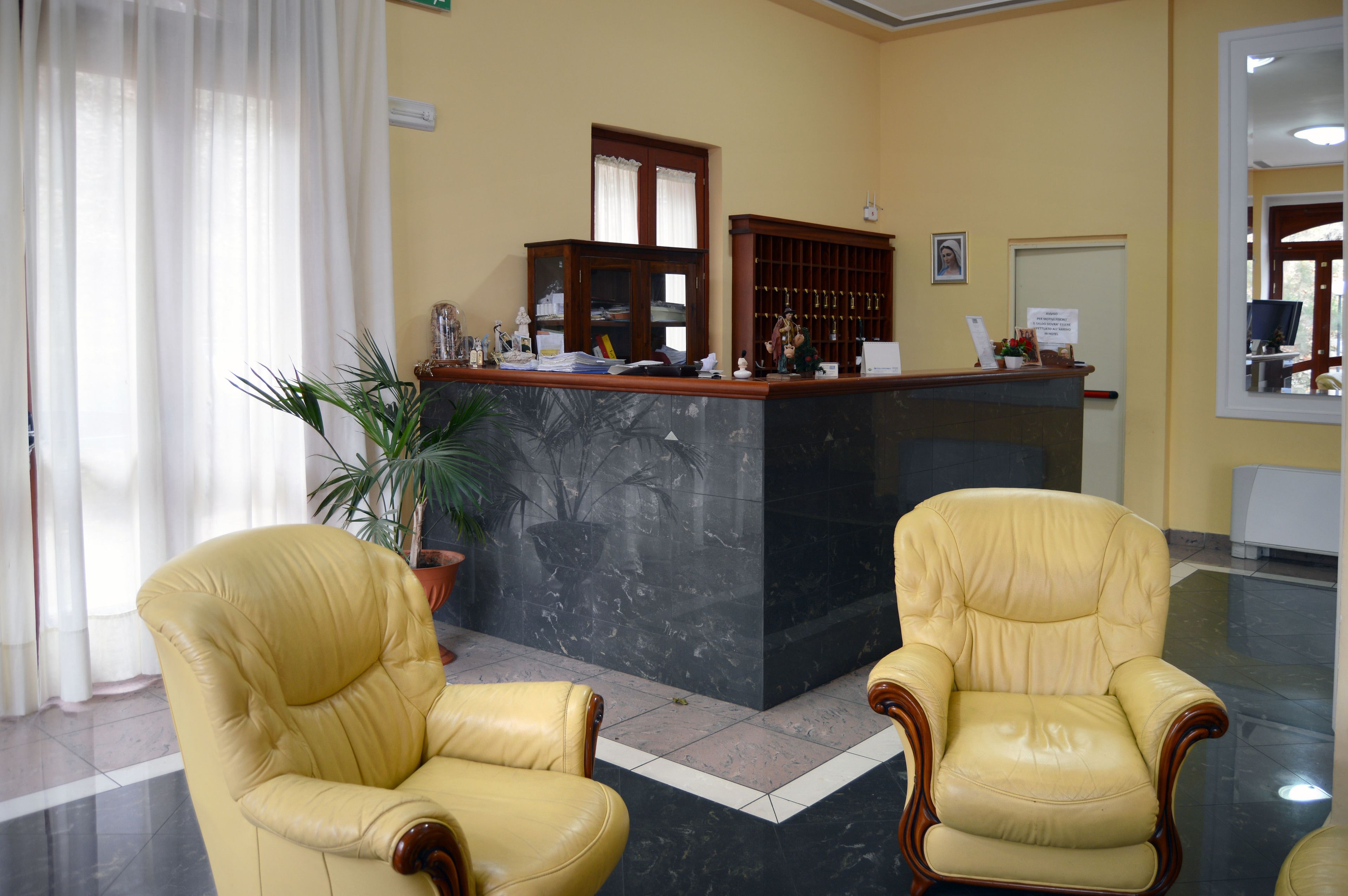 Un espace d’accueil avec un comptoir en marbre, deux fauteuils en cuir, une plante en pot et un tableau encadré au mur.