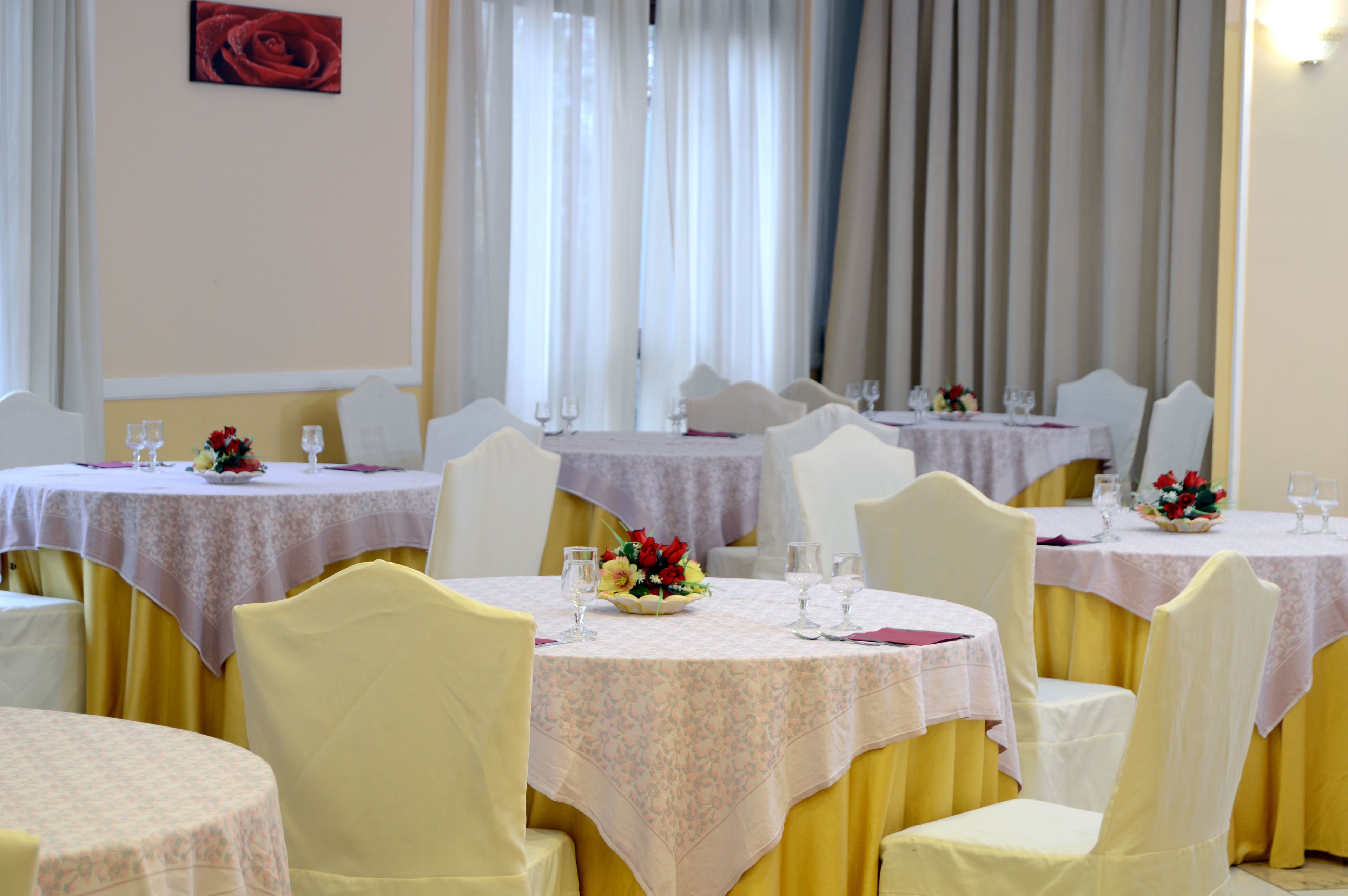 Un salón de banquetes con mesas redondas, cada una con mantel blanco, sillas amarillas y centros de mesa florales.