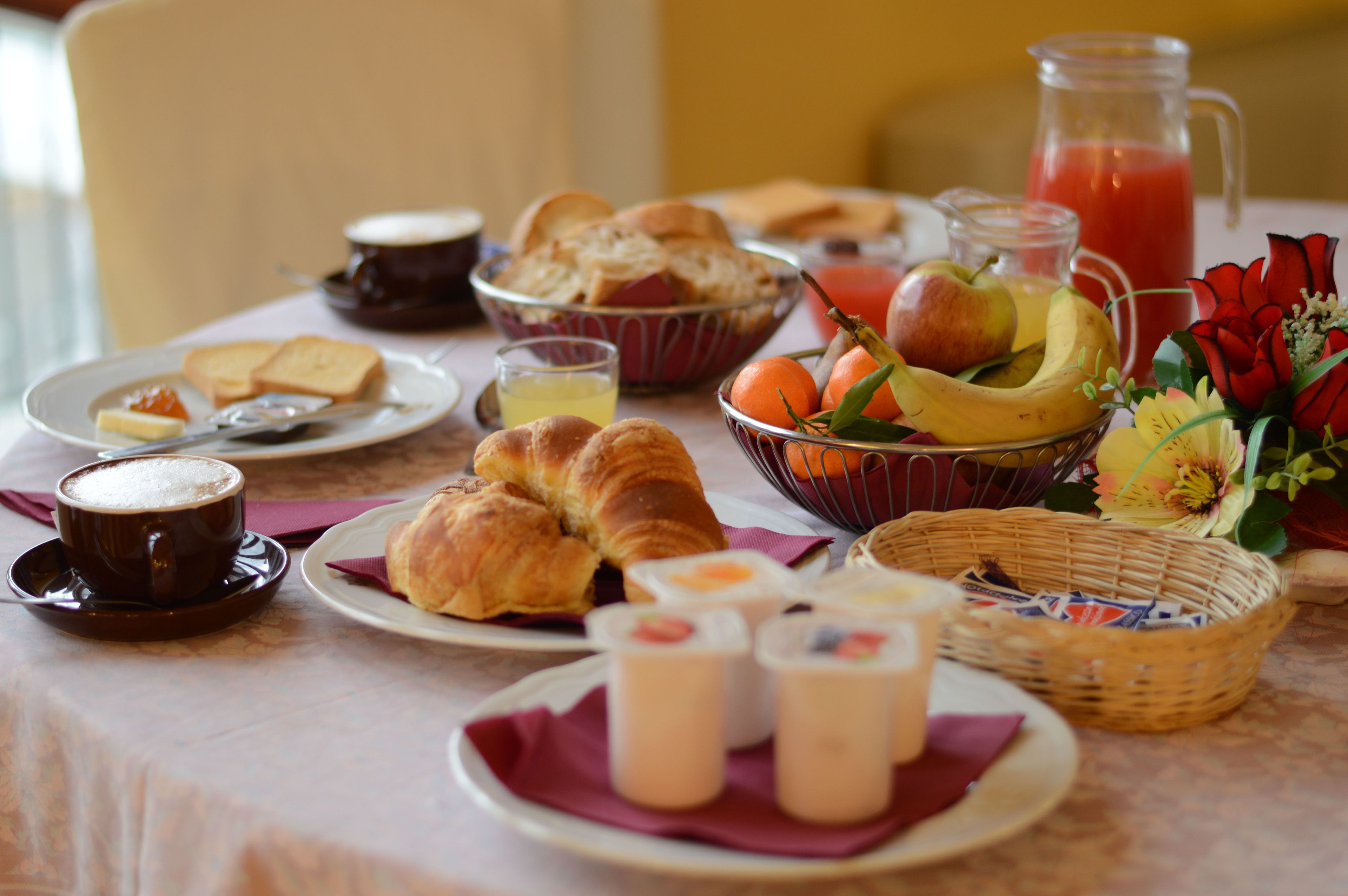 Une table de petit-déjeuner avec des croissants, du pain, des fruits, du jus et une carafe de jus d’orange.