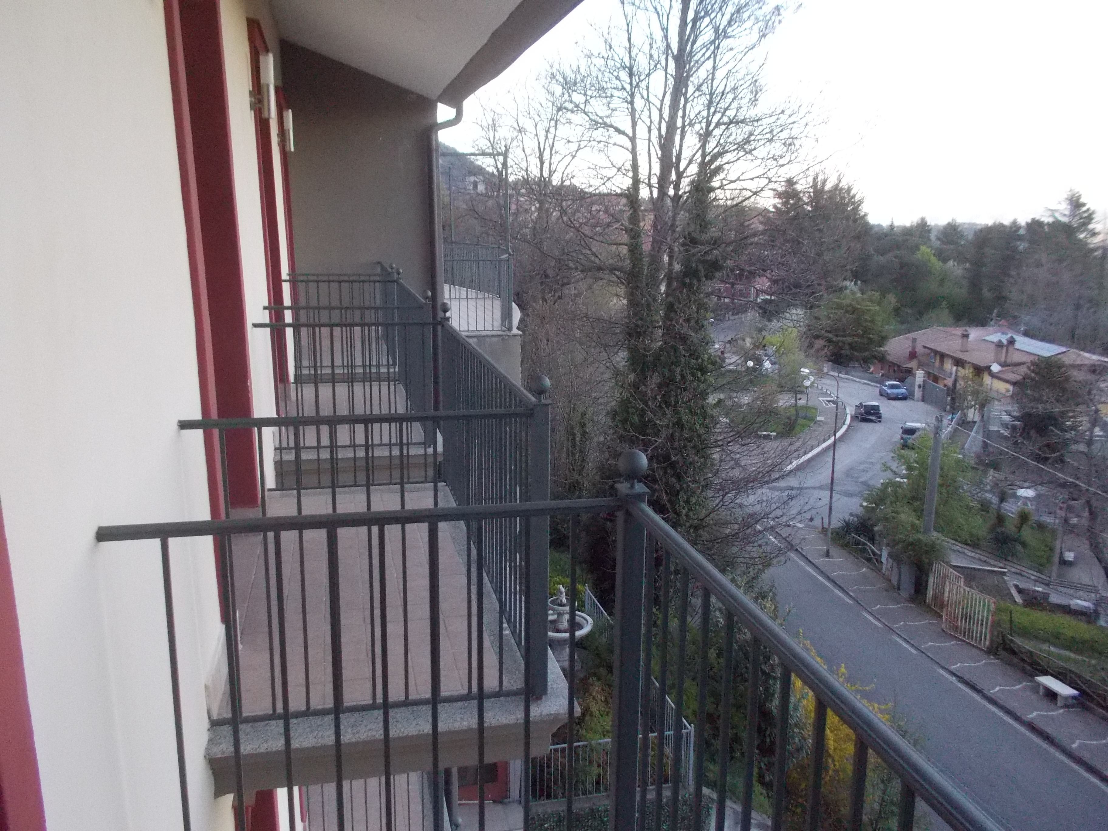 A residential building with a balcony, a staircase, and a view of a street with parked cars and houses.