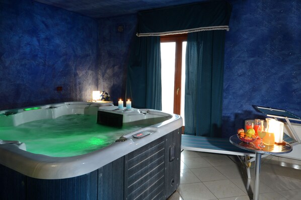 A spa room with a hot tub, candles, and a table with fruit and drinks. - Royal Hotel Montevergine (Ospedaletto D'Alpinolo)