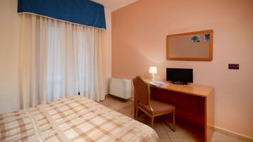 A hotel room with a bed, a desk with a computer, a chair, a lamp, and a wall-mounted mirror.