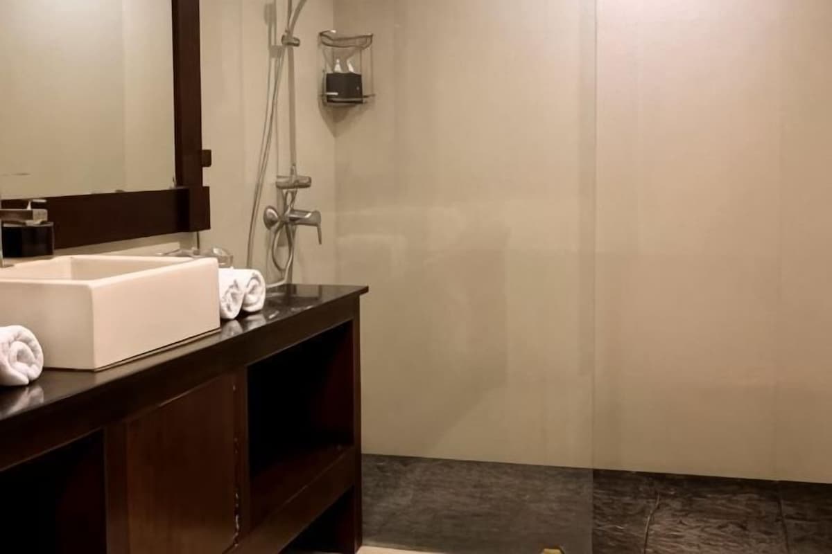 A bathroom with a white sink, dark wooden vanity, and a shower area.