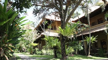 A tropical garden with a pathway leading to a building with a thatched roof and multiple balconies.
