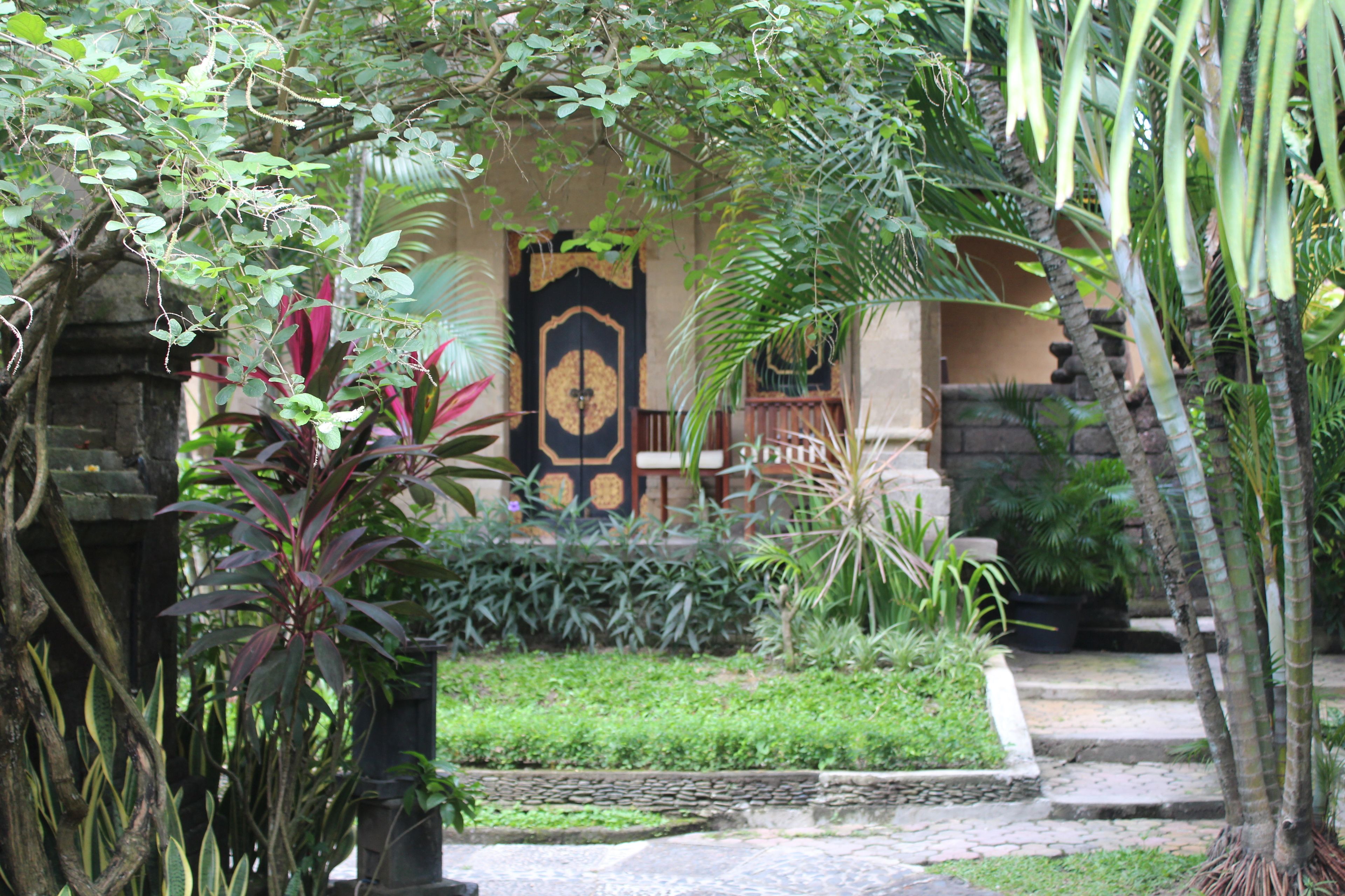 A traditional building with a black and gold door, surrounded by lush greenery and a stone pathway.