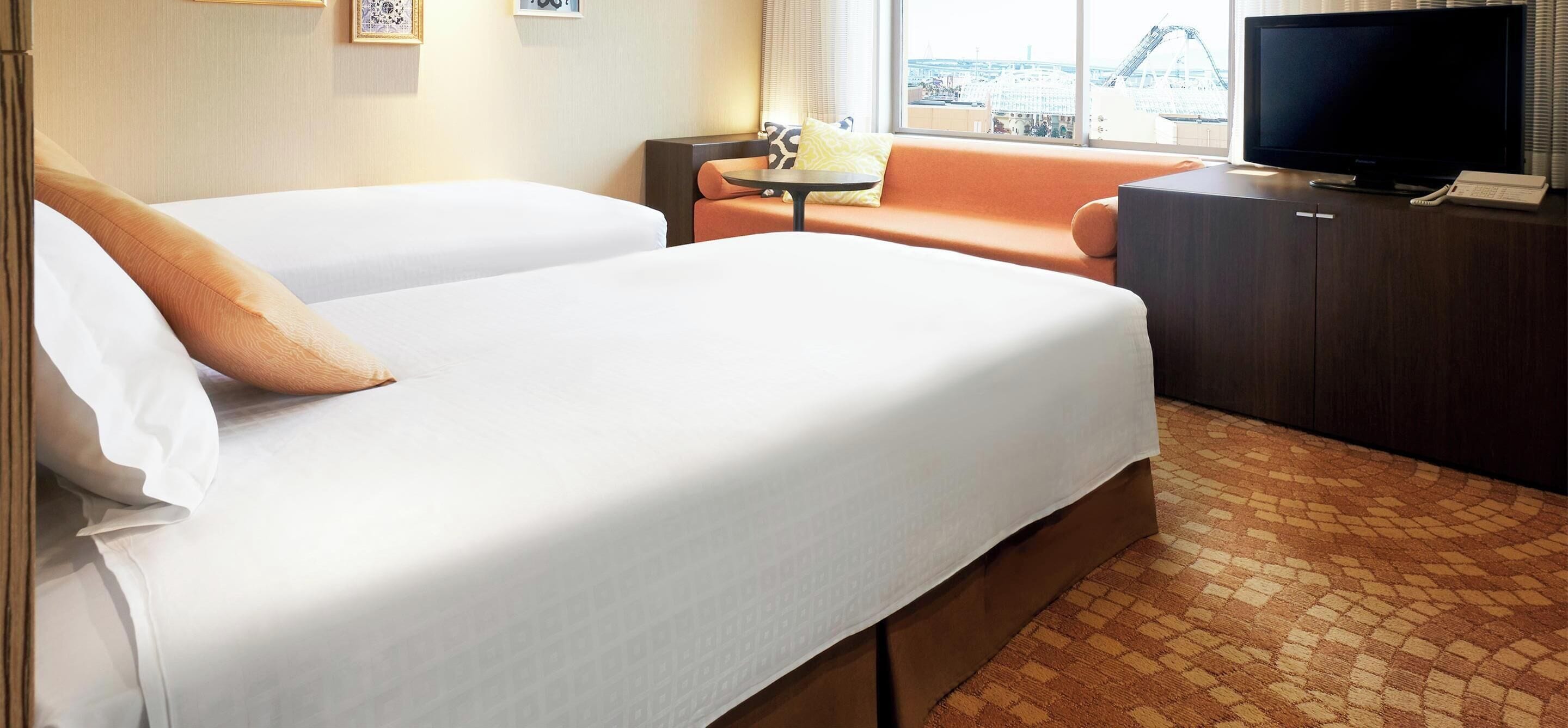 A hotel room with two beds, a television, a small table, and a view of a cityscape.