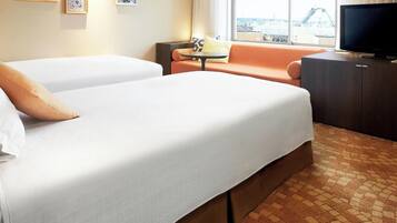 A hotel room with two beds, a television, a small table, and a view of a cityscape.