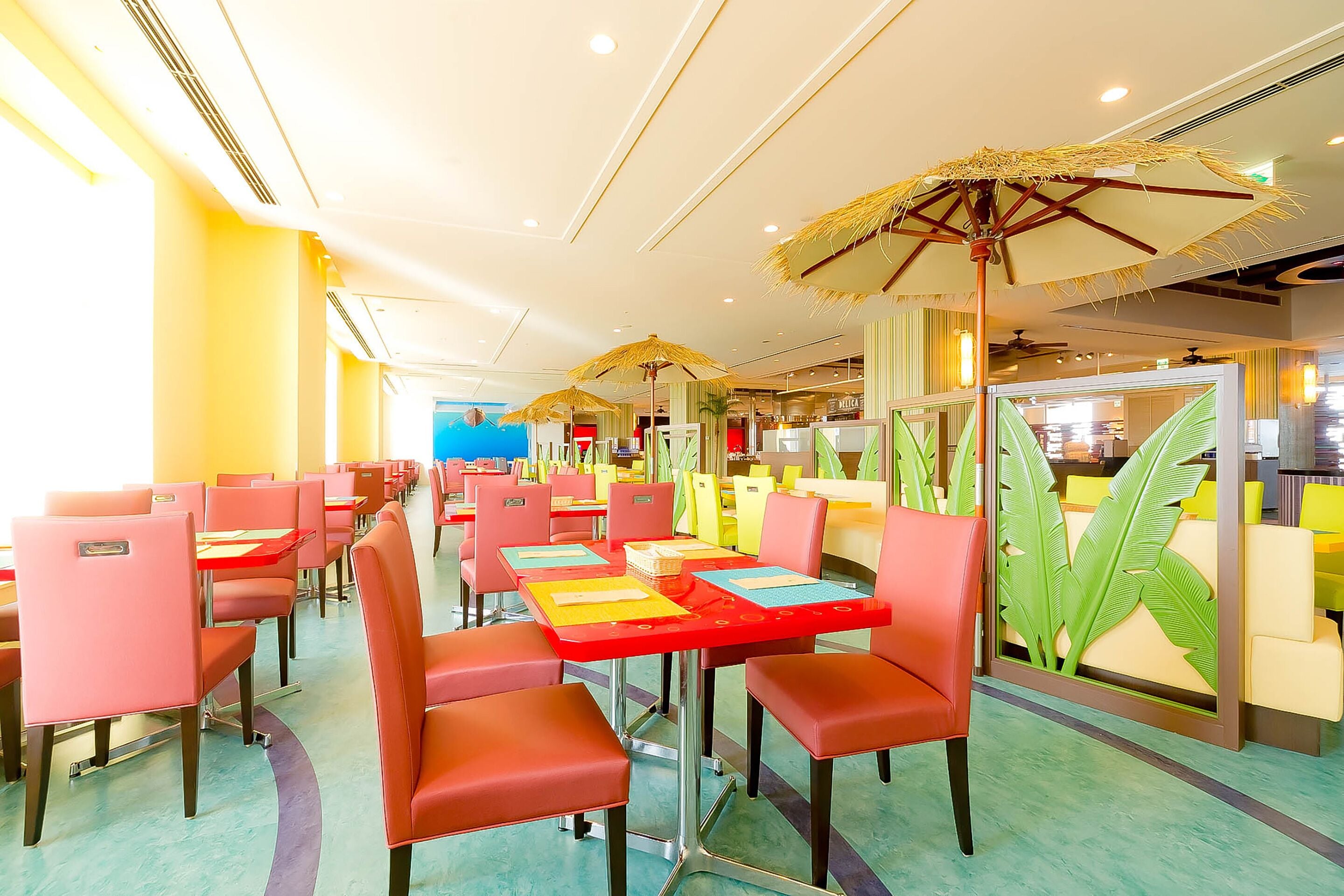 A restaurant with red and yellow tables, chairs, and a tropical-themed wall.