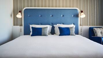 A neatly made bed with a blue headboard, two bedside lamps, and a blue chair.