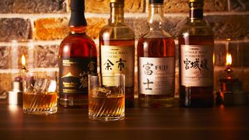 A selection of whiskey bottles and glasses on a wooden surface with a brick wall background.