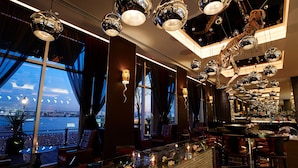 Eine moderne Bar mit glänzenden, kugelförmigen Leuchten, Blick auf die Stadt durch große Fenster und verschiedenen Sitzmöglichkeiten.