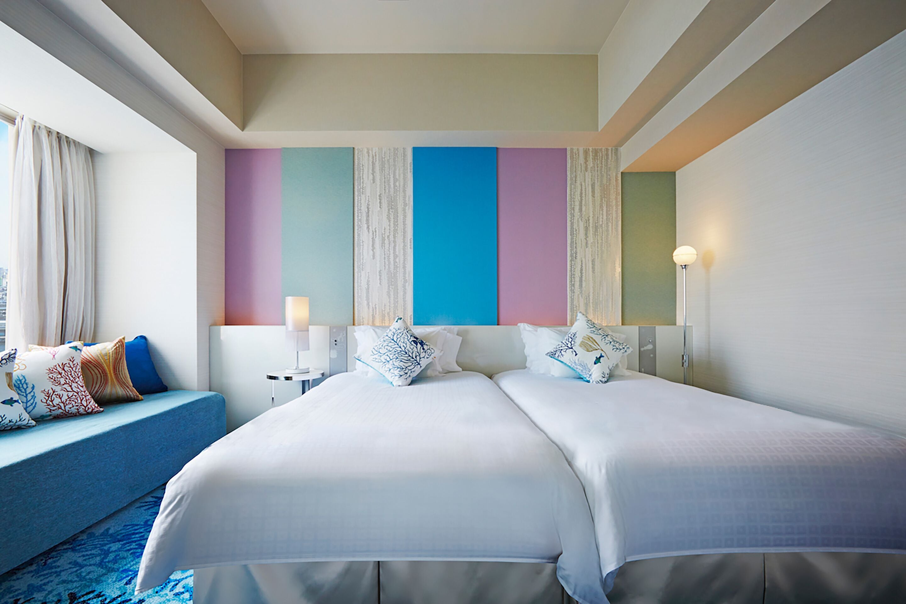 A hotel room with two beds, a blue sofa, and a large window with curtains.