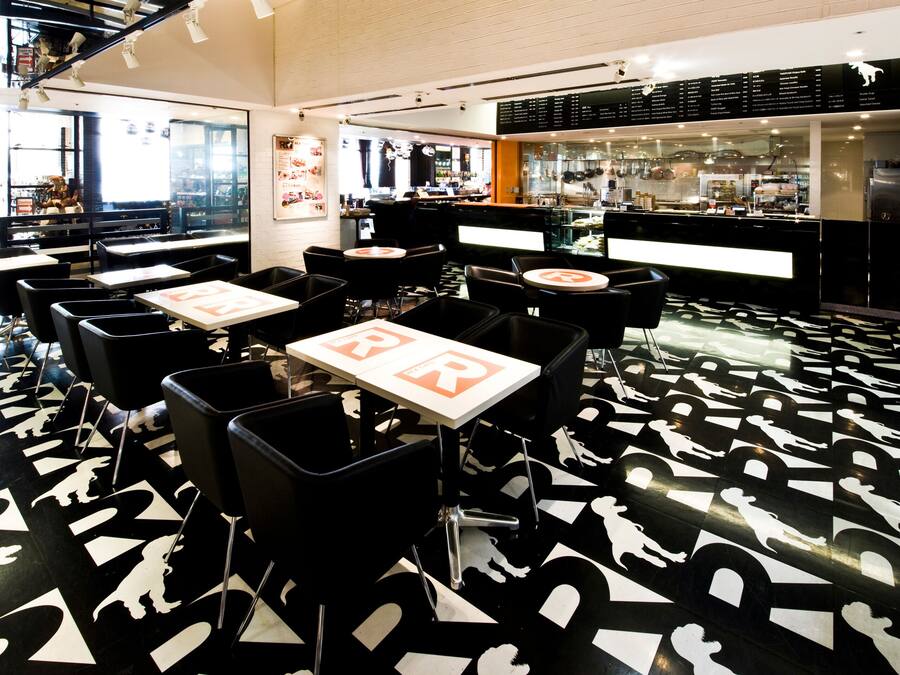 Ein Restaurant mit schwarz-weiß gemustertem Boden, Tischen mit 'BR'-Schildern und einer Bar im Hintergrund.