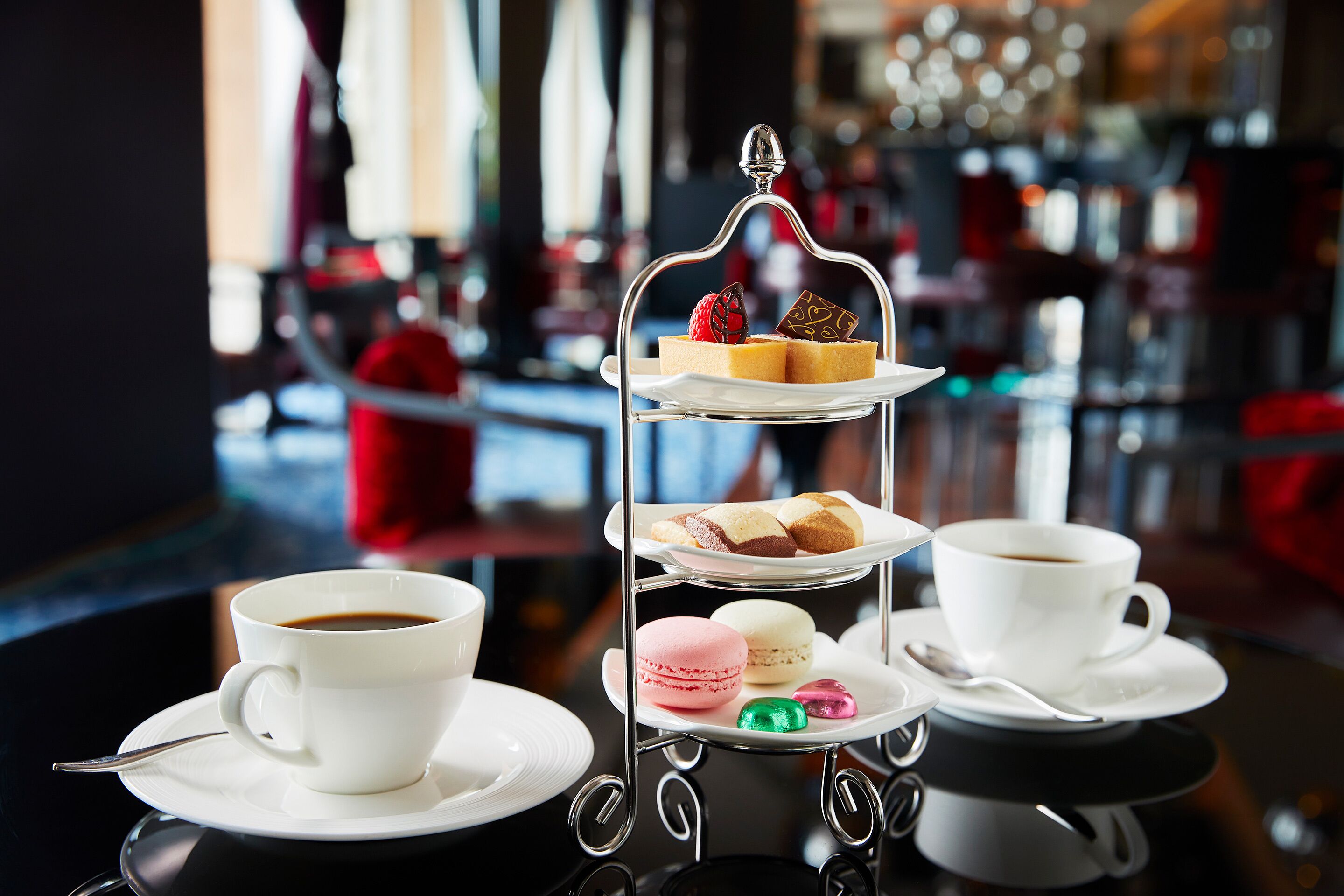 Un expositor de tres niveles con pasteles y macarons sobre una mesa en un café.