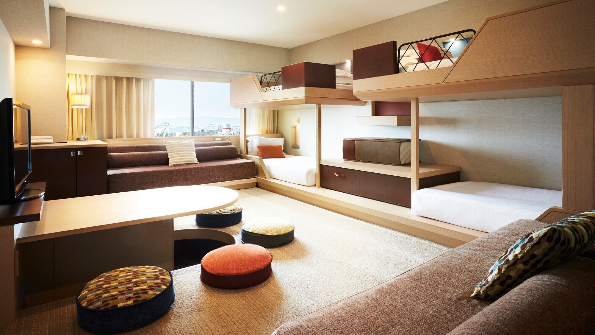 Habitación de hotel moderna con sofá, pufs, televisión y vistas a la ciudad.