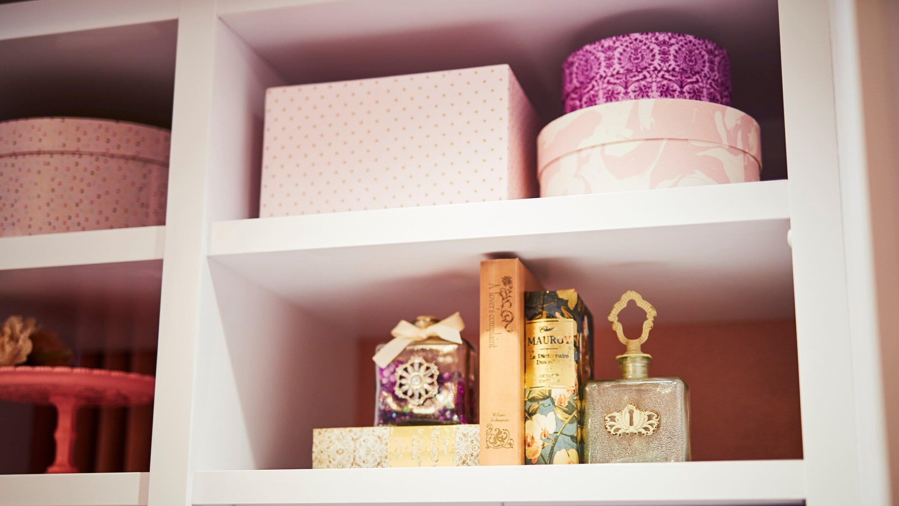 A shelf with various items including a polka-dotted box, a pink box with a bow, a book titled 'MAUROV,' a perfume bottle, and a decorative box.