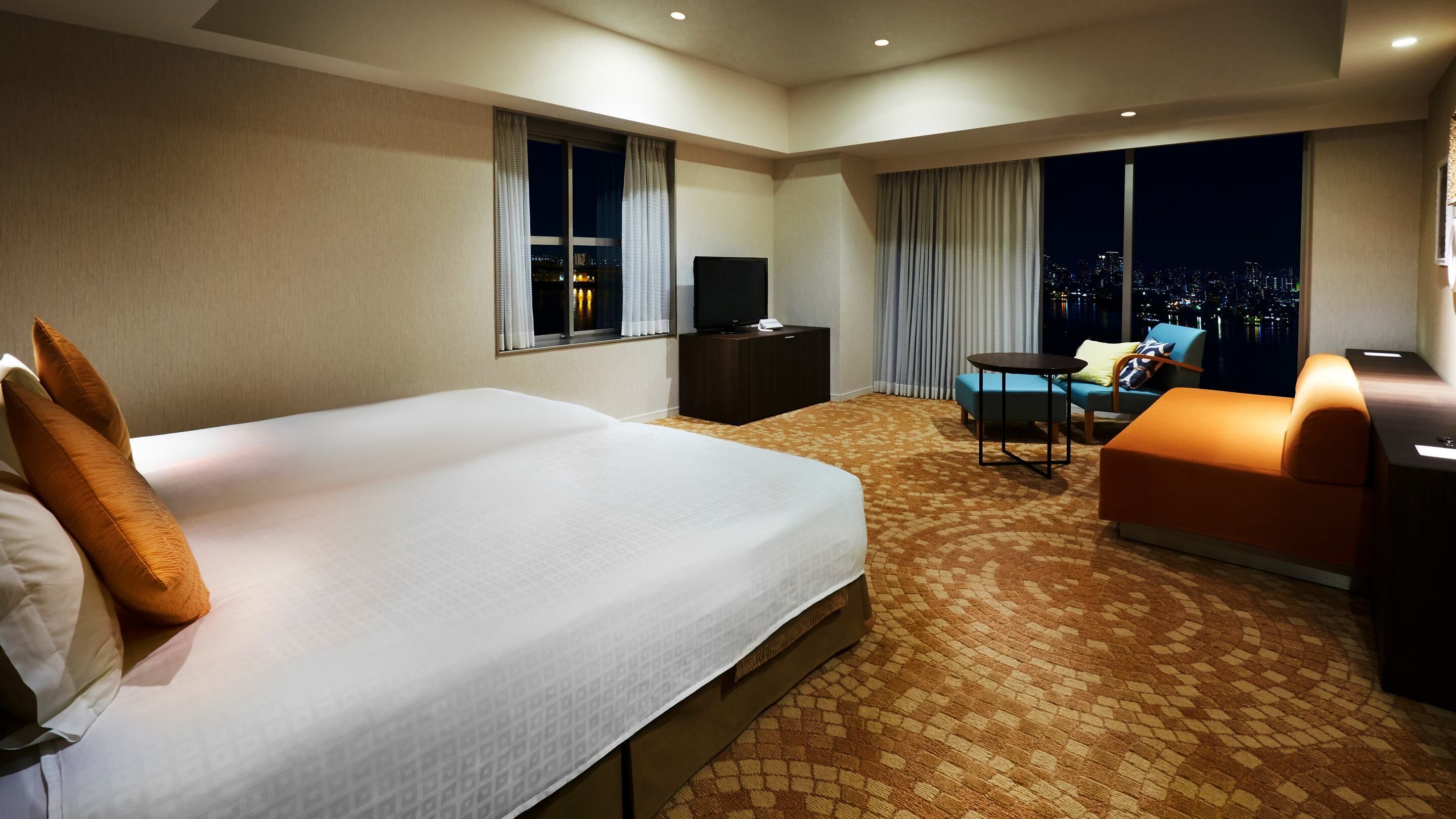 A hotel room with a large bed, a TV, a desk, a chair, and a sofa.