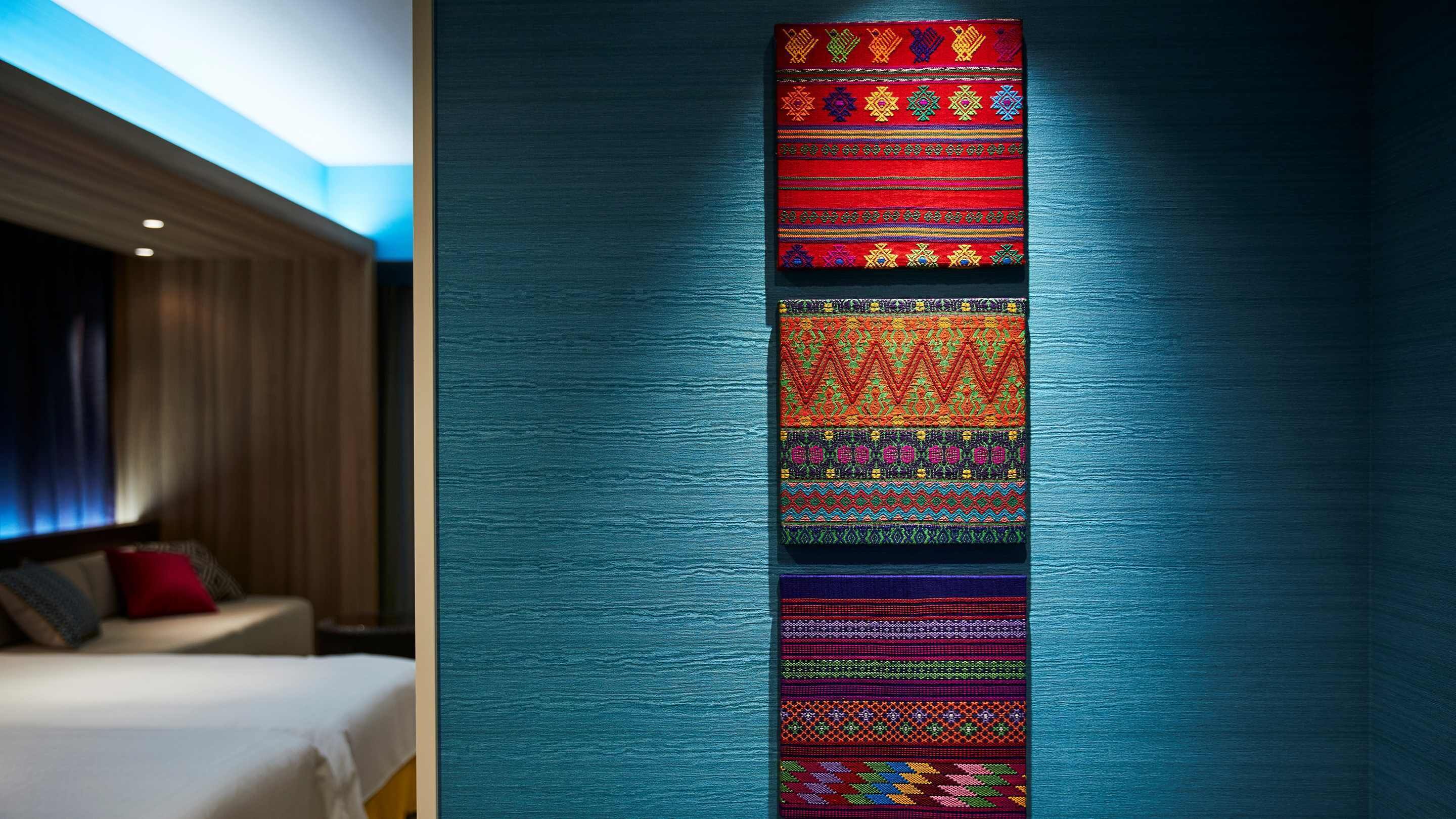 A hotel room with a bed, a nightstand, and a wall-mounted tapestry.