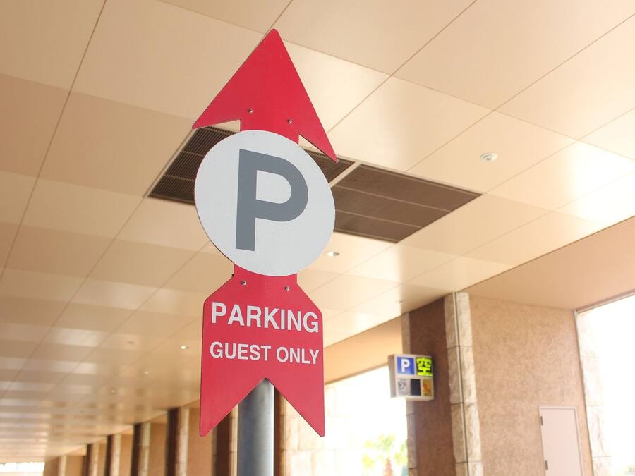 Señal de estacionamiento exclusivo para huéspedes con una flecha direccional, un techo con iluminación empotrada y vistas a palmeras.