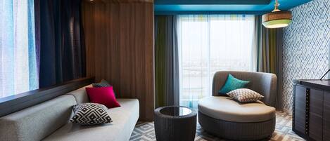 A modern hotel room with a sofa, ottoman, and a round table.