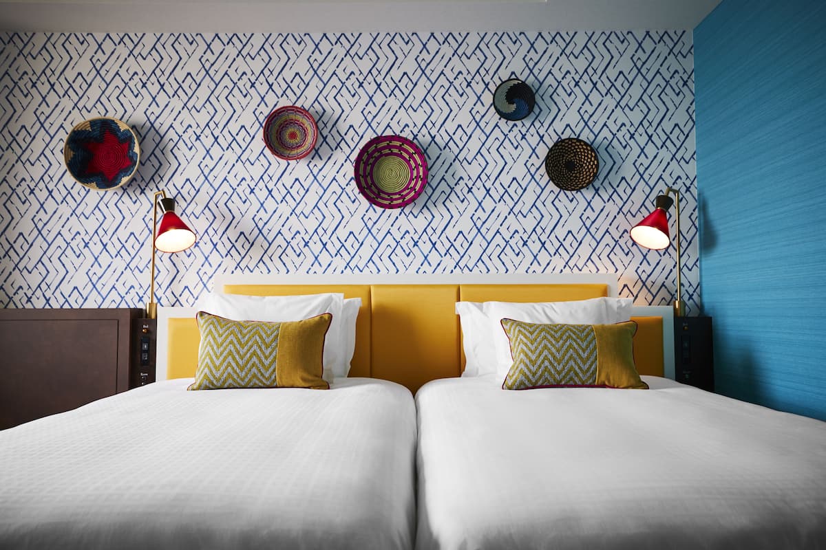 Una cama doble con dos almohadas, un cabecero y una pared con papel tapiz estampado y platos decorativos.