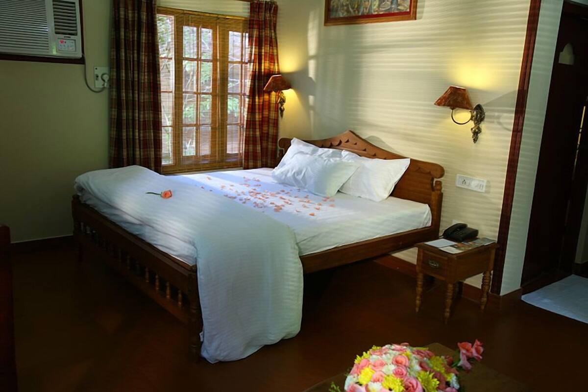 A bedroom with a wooden bed, two bedside lamps, a nightstand, and a window with curtains.