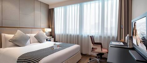 A modern hotel room with a large bed, a desk, and a television.