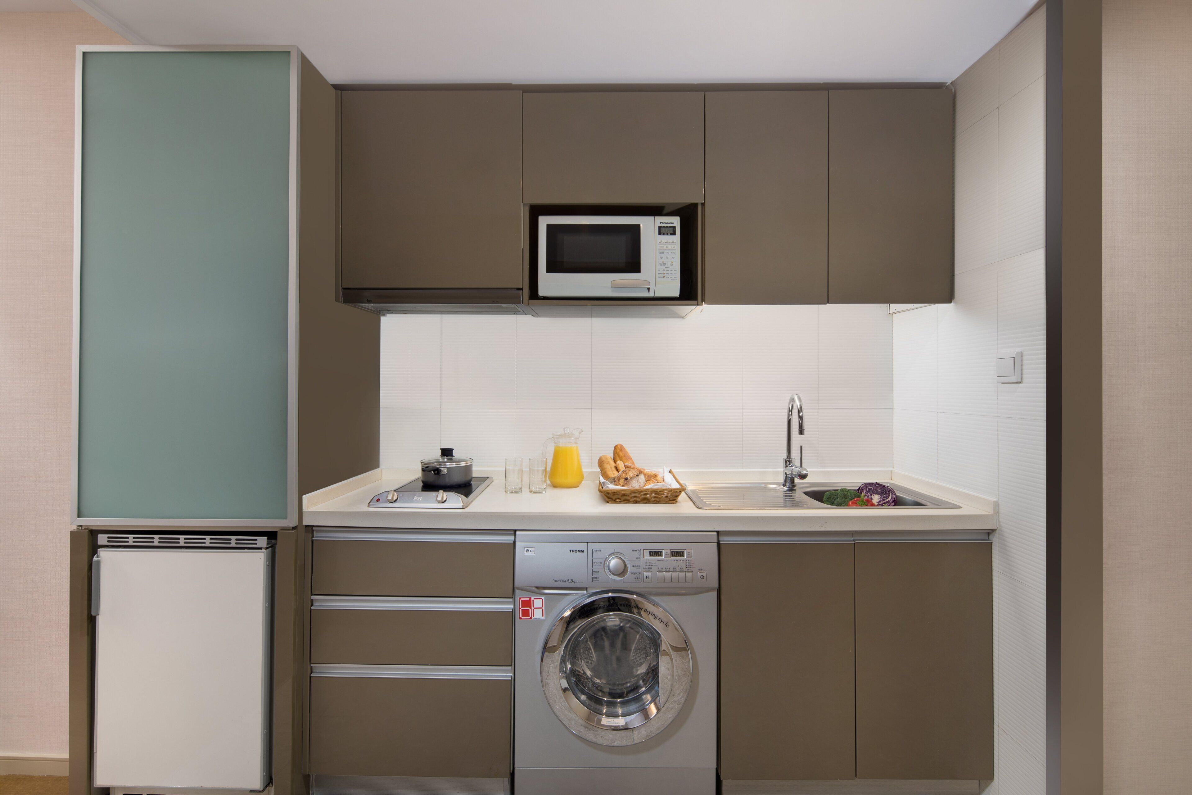 A compact kitchen with a microwave, sink, and washing machine.