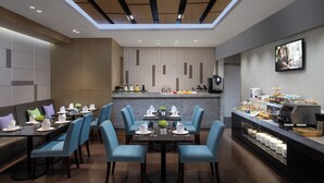 Een moderne eetruimte met een centrale tafel voor vier personen, omringd door blauwe stoelen, en een buffet aan de rechterkant.