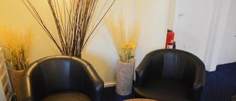A room with two black leather chairs, a round wooden table, and decorative plants.