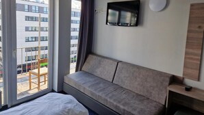 Habitación de hotel moderna con un ventanal grande, un sofá, un televisor de pantalla plana y una mesita de madera.