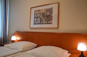 A hotel room with a wooden headboard, two beds with white linens, two bedside lamps, and a framed picture of a building on the wall. - Hotel Mercedes Hamburg (Hamburg)