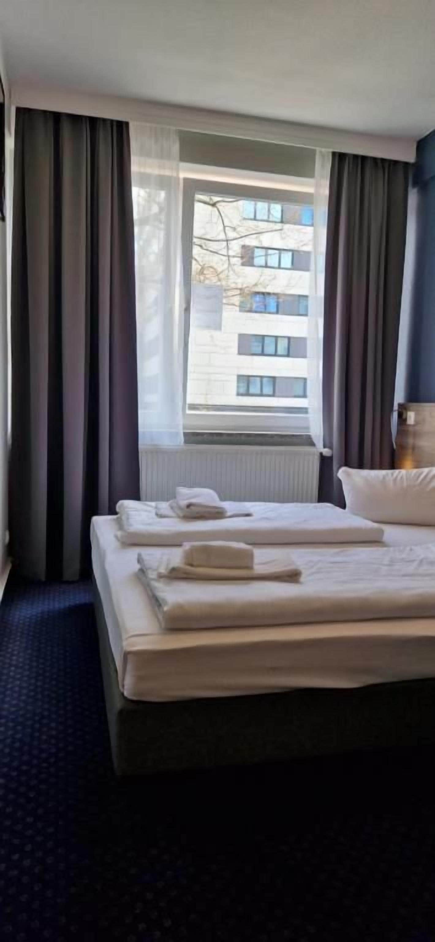 Une chambre d’hôtel avec un lit, une fenêtre avec des rideaux et une vue sur un bâtiment à l’extérieur.