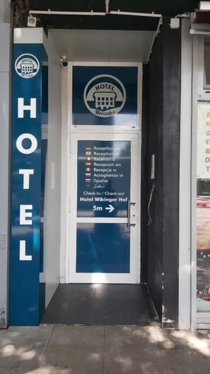 Een hotelentree met een receptiebalie, een bordje dat in- en uitchecken bij Hotel Vikinger Hof aangeeft, en een blauw verticaal bord met de tekst 'HOTEL'.